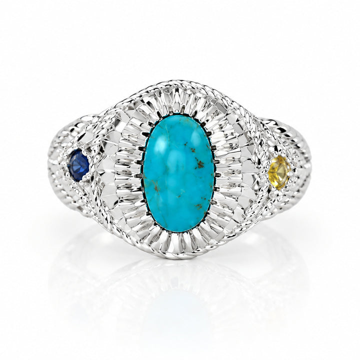 A vintage-style Art Deco ring featuring a central oval turquoise cabochon surrounded by a halo of small clear stones, accented with a small blue gemstone on one side and a tiny yellow gemstone on the other, set against a plain light gray background.